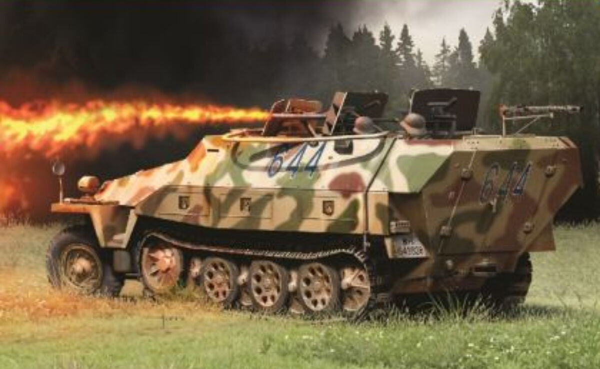 A German military armoured vehicle with a green, brown, and tan camouflage pattern is shown in a grassy field with a forest in the background. The vehicle is emitting a bright orange fire or explosion effect from its side, with smoke and dark trees behind it.