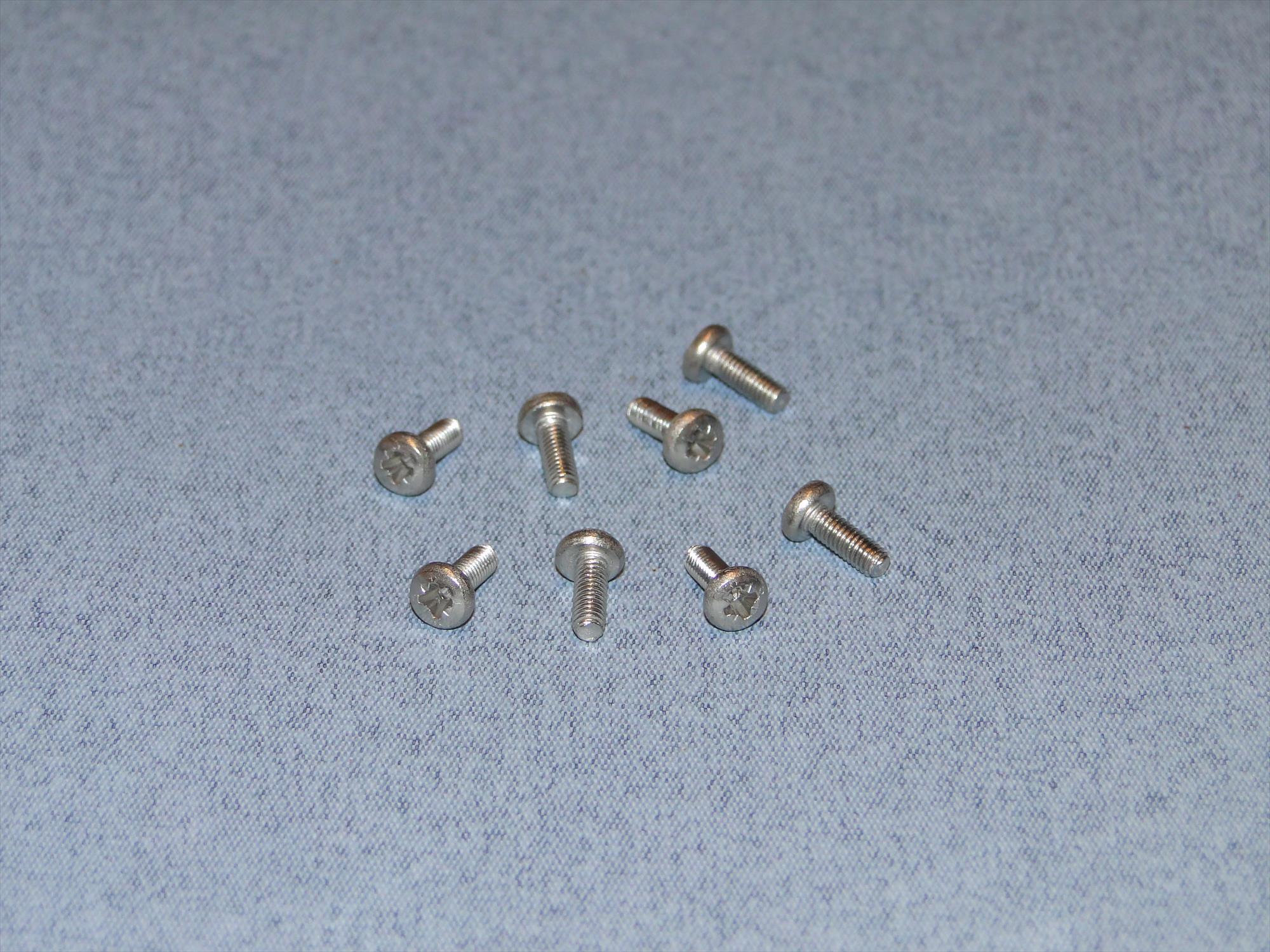 8 small silver metal screws arranged on a textured light blue fabric background.