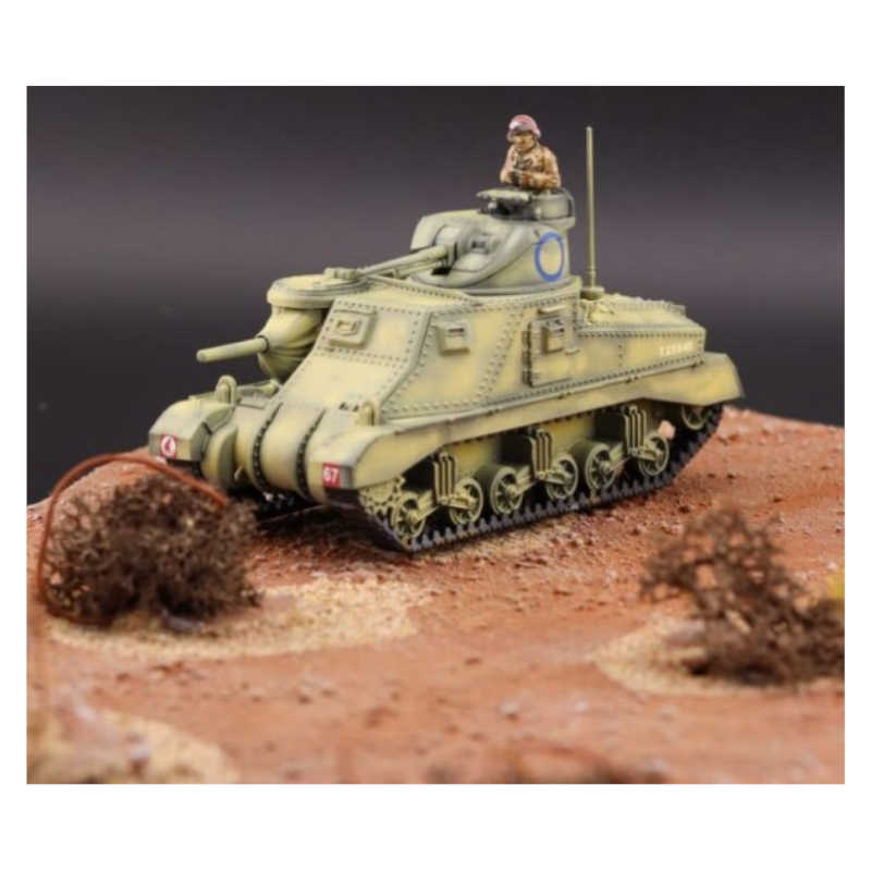 A painted military tank model displayed on a textured desert-style diorama base with small bushes, photographed against a dark studio background.